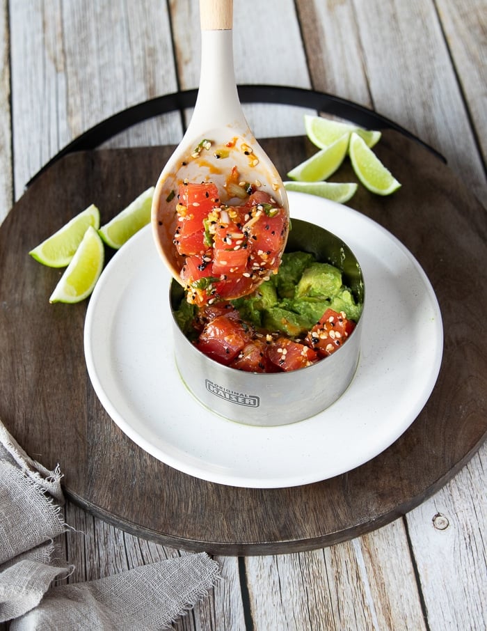 a spoon adding in a layer of tuna tartare over the avocado layer