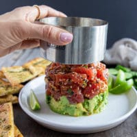 A hand removing the mold from the layered tuna tartare showing the layer of tuna and avocado