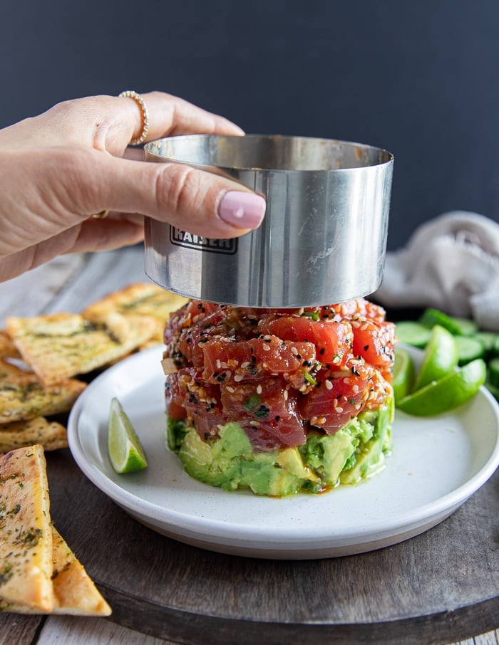 A hand removing the mold from the layered tuna tartare showing the layer of tuna and avocado