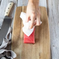 a hand with a kitchen towel patting down the tuna to dry it