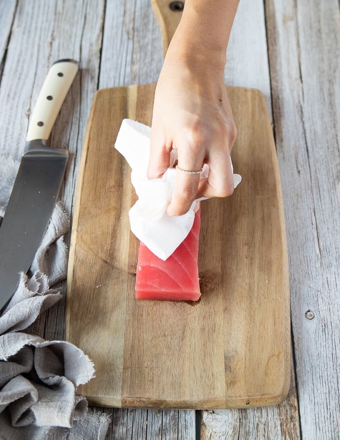 a hand with a kitchen towel patting down the tuna to dry it