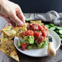 A hand scooping out tuna and avocado using pita chips