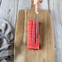 a hand cutting up the tuna steak using a knife