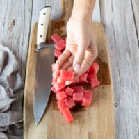 A hand holding a chunk of cut up fresh ahi tuna showing the size of the chunks