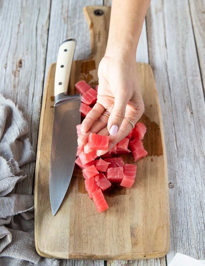 A hand holding a chunk of cut up fresh ahi tuna showing the size of the chunks