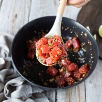 a spoon mixing in the fresh tuna chunks into the bowl with the marinade