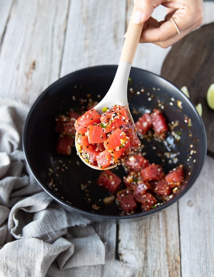 a spoon mixing in the fresh tuna chunks into the bowl with the marinade