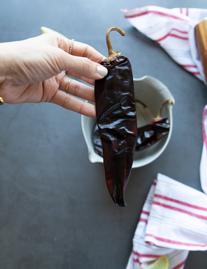 a hand holding a Guajillo chilli to show the pepper