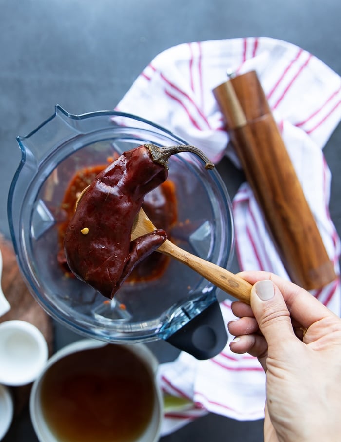 a hand adding in the soaked and ready Guajillo chillies into the blender for the sauce