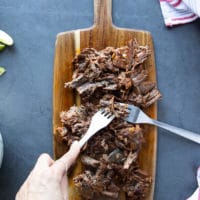 two forks are used to shred the birria meat on a wooden board