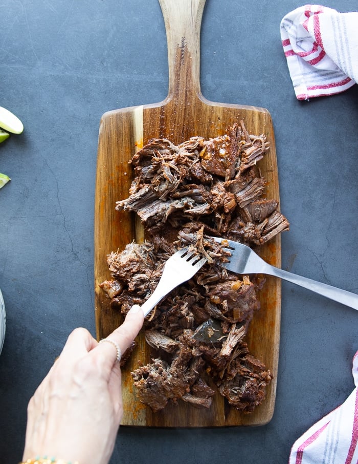 two forks are used to shred the birria meat on a wooden board