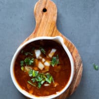 a bowl of birria dipping sauce with white onions and cilantro