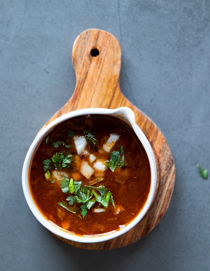 a bowl of birria dipping sauce with white onions and cilantro