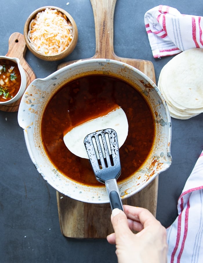 a hand dipping the tortilla into the birria sauce before making the tacos