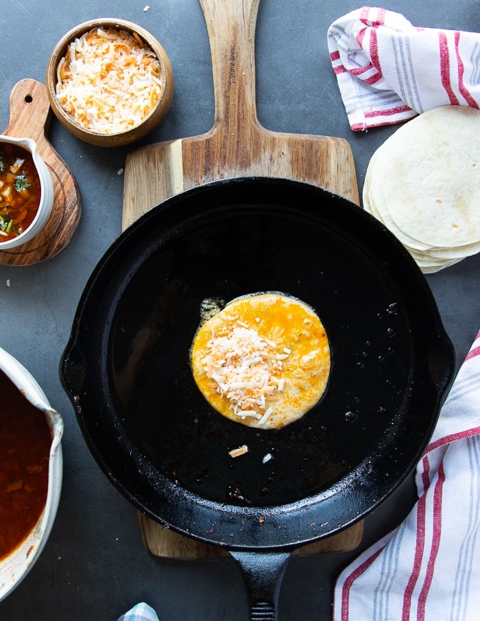 the dipped tortilla in a pan with cheese placed on one half of it