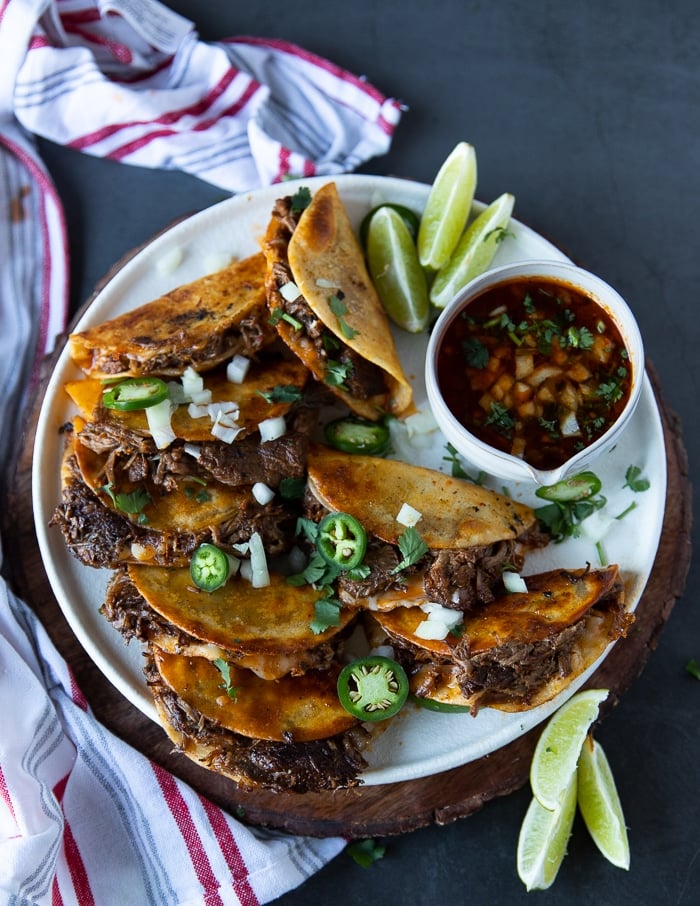 A plate of birria tacos with a bowl of dipping sauce next to it