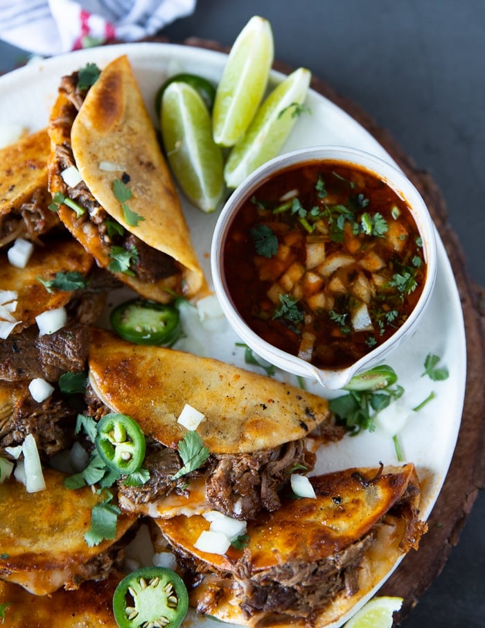 Crispy Birria tacos on a plate showing how crispy the edges are and with a close up of the dipping sauce