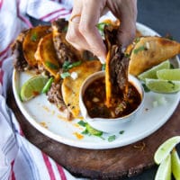 a hand dipping a birria tacos in the birria sauce