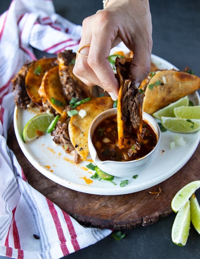 a hand dipping a birria tacos in the birria sauce