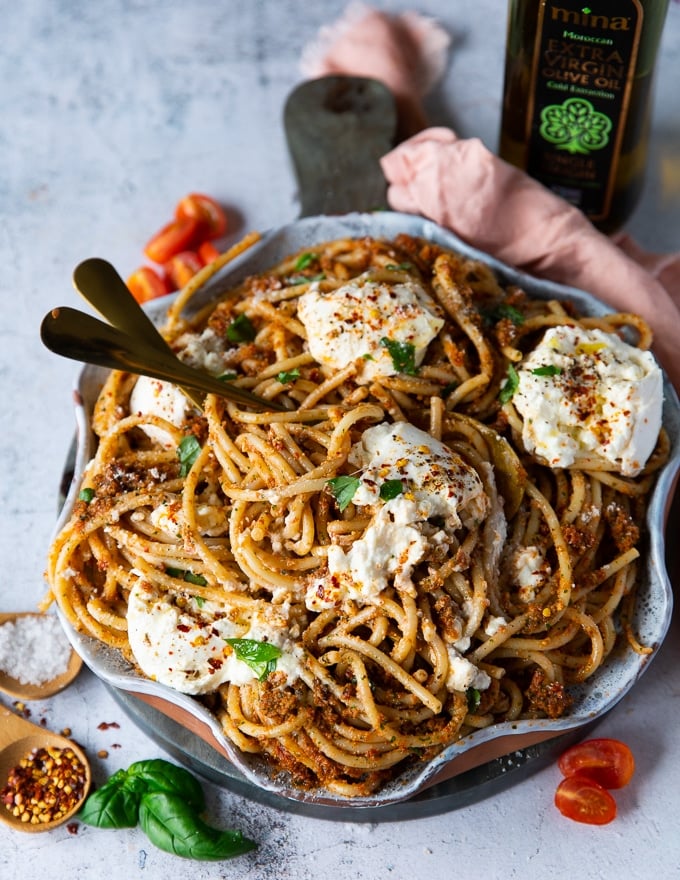 two spoons breaking up the burrata cheese over the pasta