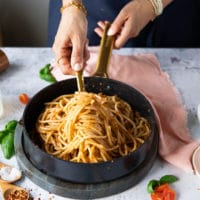 A hand tossing the pasta in a pan with the pesto and adding pasta water until the sauce is thick