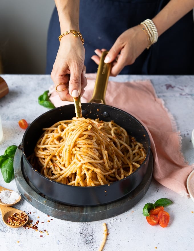 A hand tossing the pasta in a pan with the pesto and adding pasta water until the sauce is thick