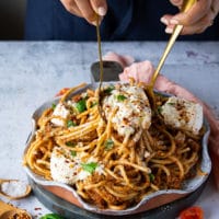 two spoons serving and tossing the burrata pasta and serving it.