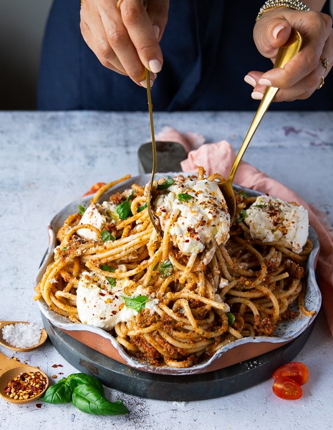 two spoons serving and tossing the burrata pasta and serving it. 