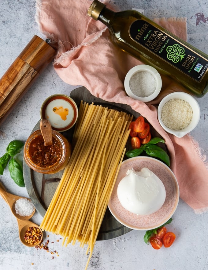 ingredients for burrata pasta including burrata cheese, pesto, salt, raw pasta, fresh basil, salt, parmesan cheese