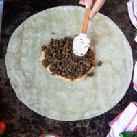 A hand adding in some cooked ground beef