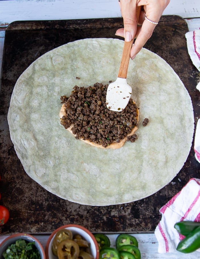 A hand adding in some cooked ground beef