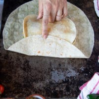 the process of folding the crunchwrap supreme starting with one hand folding one side of the large tortilla