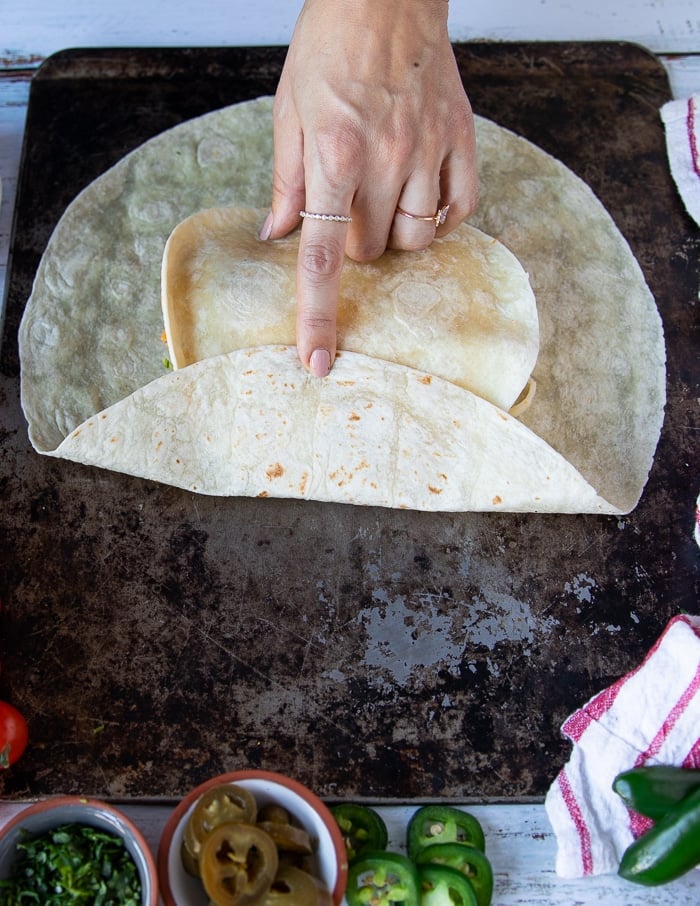 the process of folding the crunchwrap supreme starting with one hand folding one side of the large tortilla