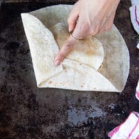 process of folding the crunchywrap supreme with one hand holding firm one part of the tortilla and the other side being folded over