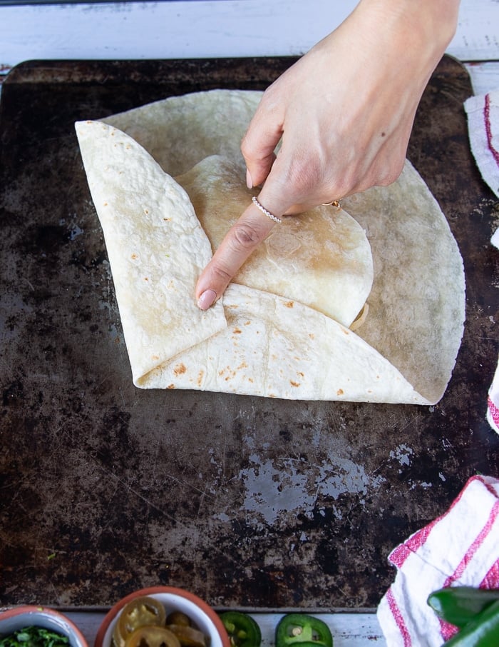 process of folding the crunchywrap supreme with one hand holding firm one part of the tortilla and the other side being folded over