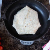 the crunchwrap supreme being placed seam side down on a skillet to cook and melt the cheese