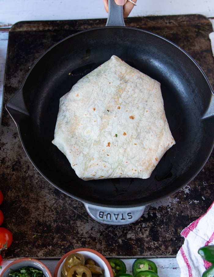 the crunchwrap supreme being placed seam side down on a skillet to cook and melt the cheese