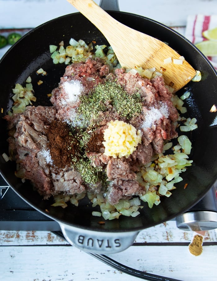 all meat ingredients added to the pan including ground beef or lamb, minced garlic, spices and seasoning