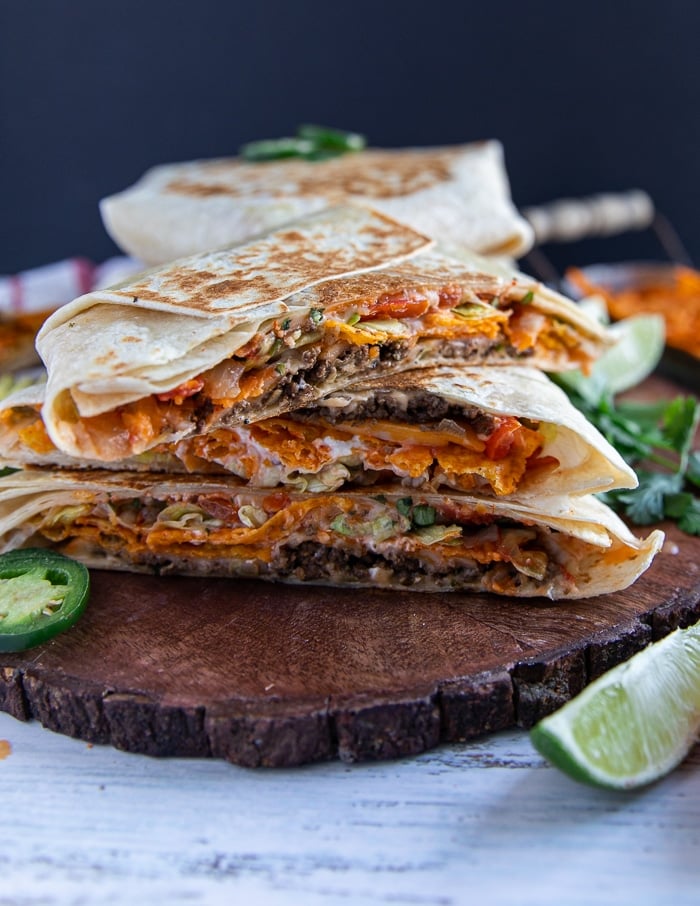 stacked up crunchwrap supreme on an angle to show the melted cheese and the different layers on a wooden board with a lime
