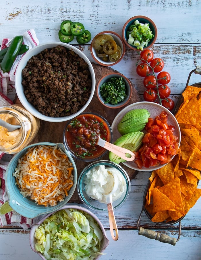 filling and layering ingredients for the cruchwrap supreme including the seasoned meat, cheese, sour cream, lettuce, tomatoes, cheese sauce, avocado, jalapeno, salsa, tostada, cilantro, scallions