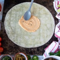 A spoon adding in some nacho cheese sauce in the middle of the large tortilla