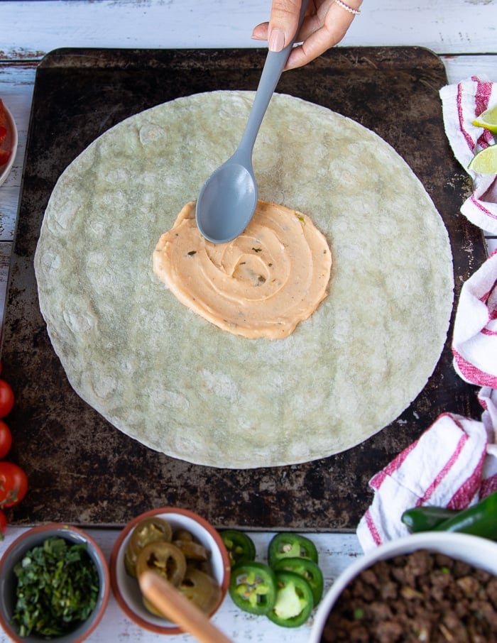 A spoon adding in some nacho cheese sauce in the middle of the large tortilla