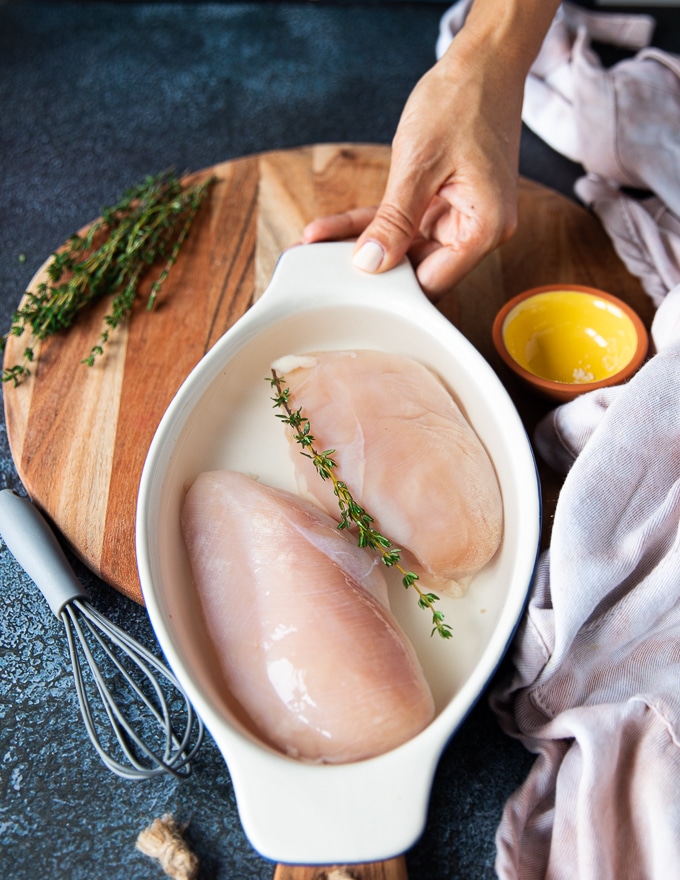 chicken breasts are placed in a bowl with the brine and a sprig of fresh thyme before air frying the4 chicken breasts
