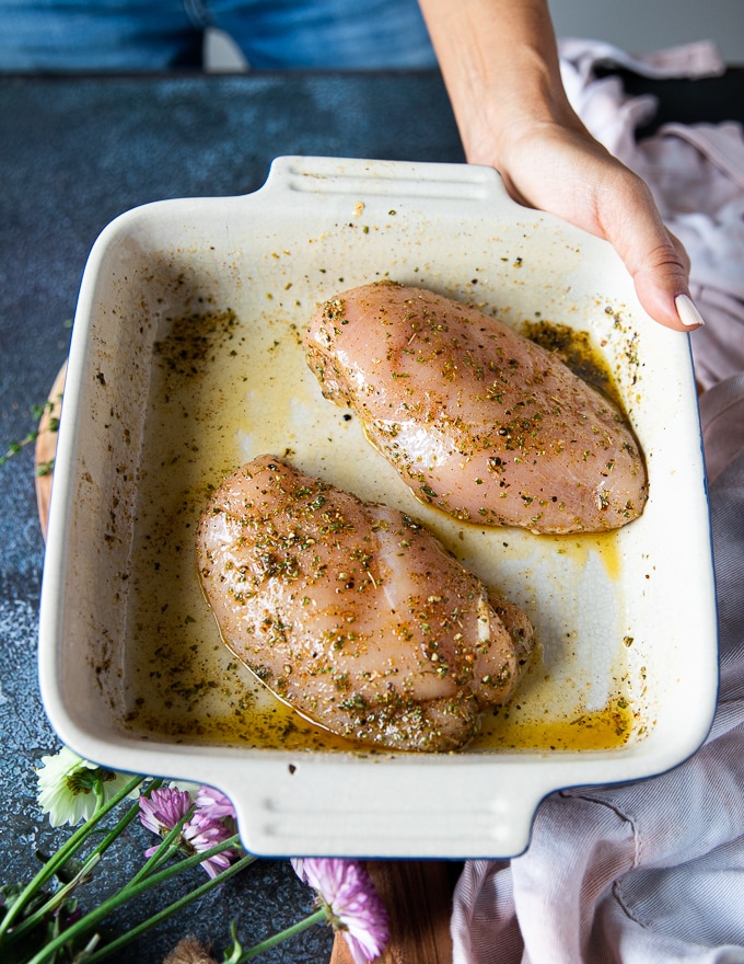 The chicken breasts placed in a plate all sprinkled with seasoning and olive oil 