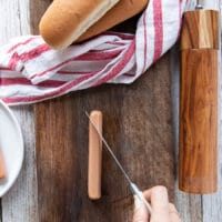 A hand holding a knife scorching the hot dogs before adding it ti the air fryer