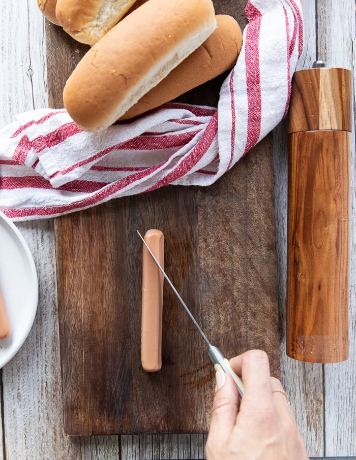 A hand holding a knife scorching the hot dogs before adding it ti the air fryer