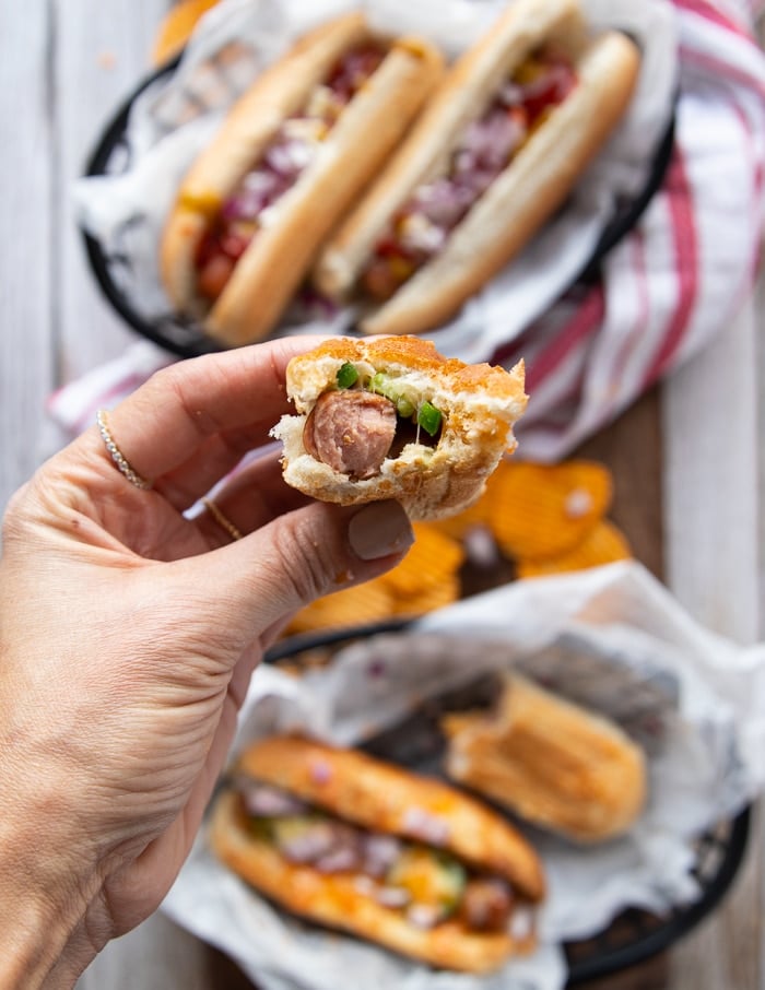 A hand holding a bitten off hot dog sandwich showing how juicy air fryer hot dogs are