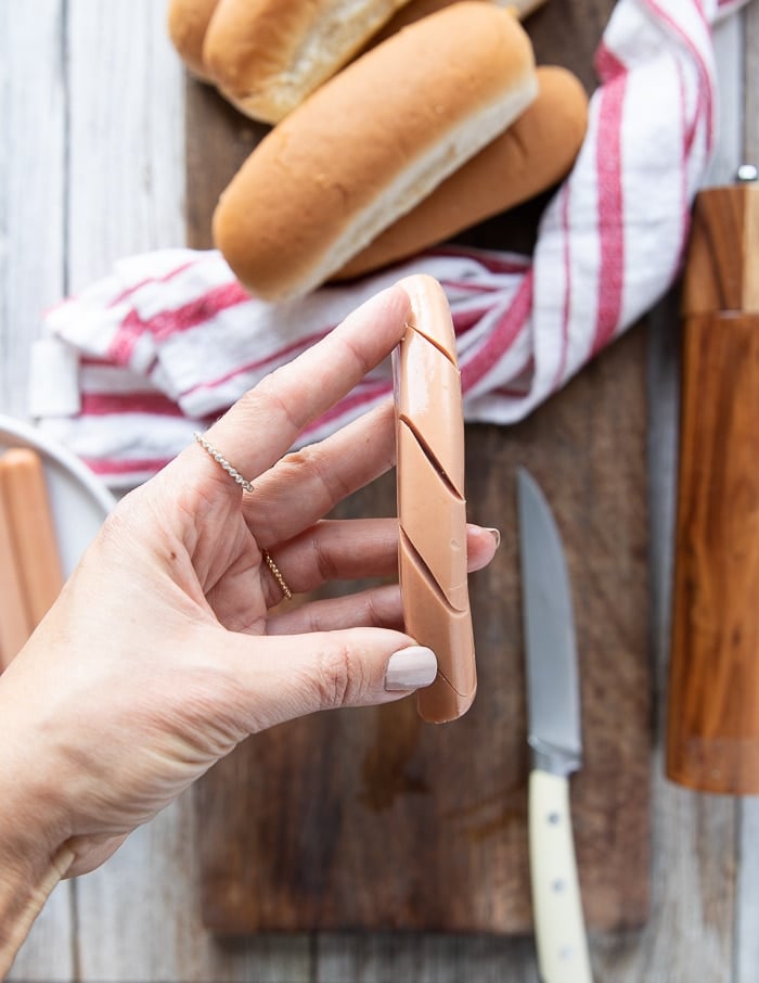 a hand holding the ready hot dogs with slits to go in the air fryer