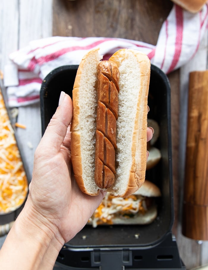 a hand holding a toasted bun and a cooked hot dog