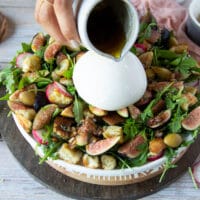 A hand pouring the balsamic salad dressing over the burrata cheese salad